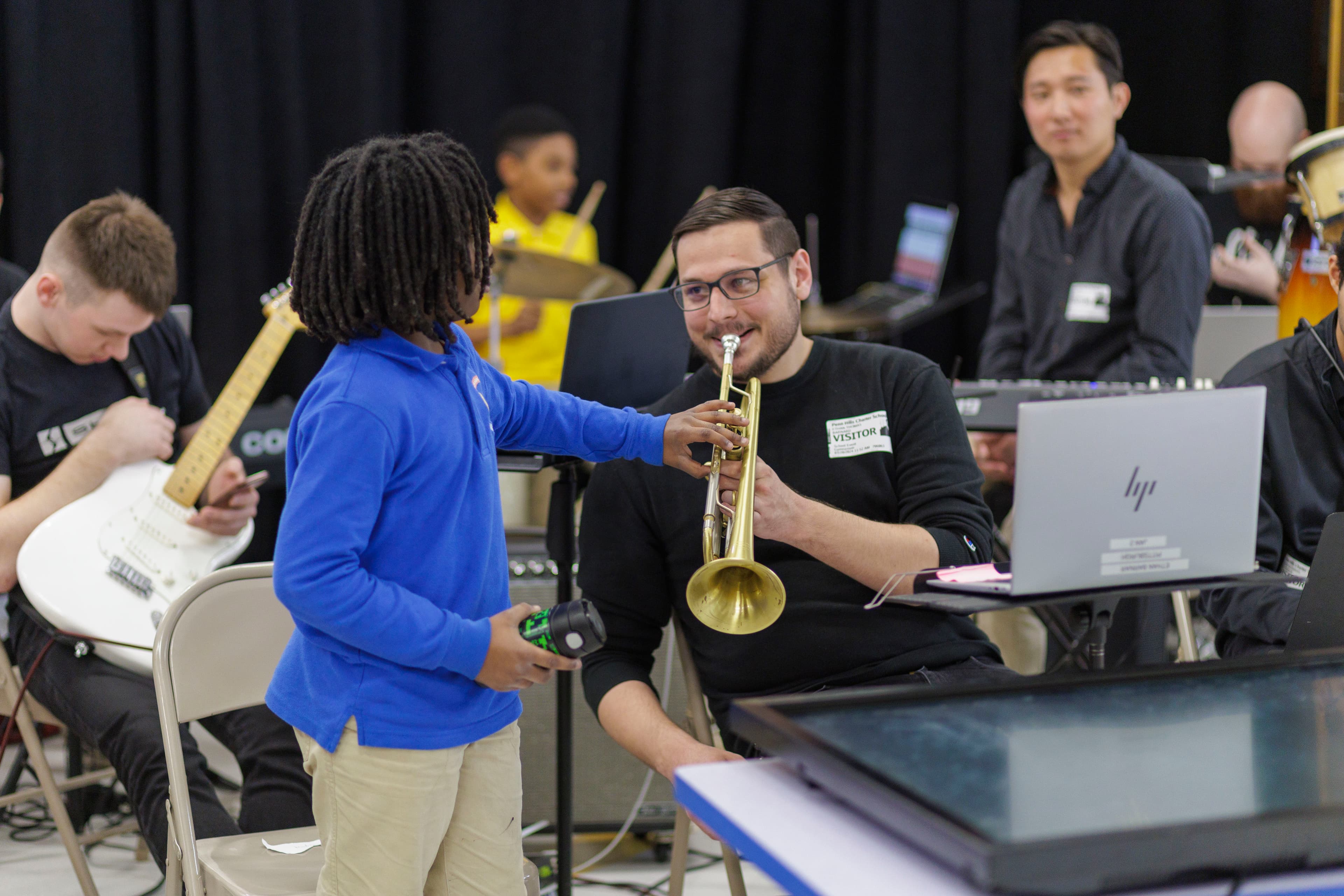 A student stands beside the trumpet player who is about to perform the song they wrote